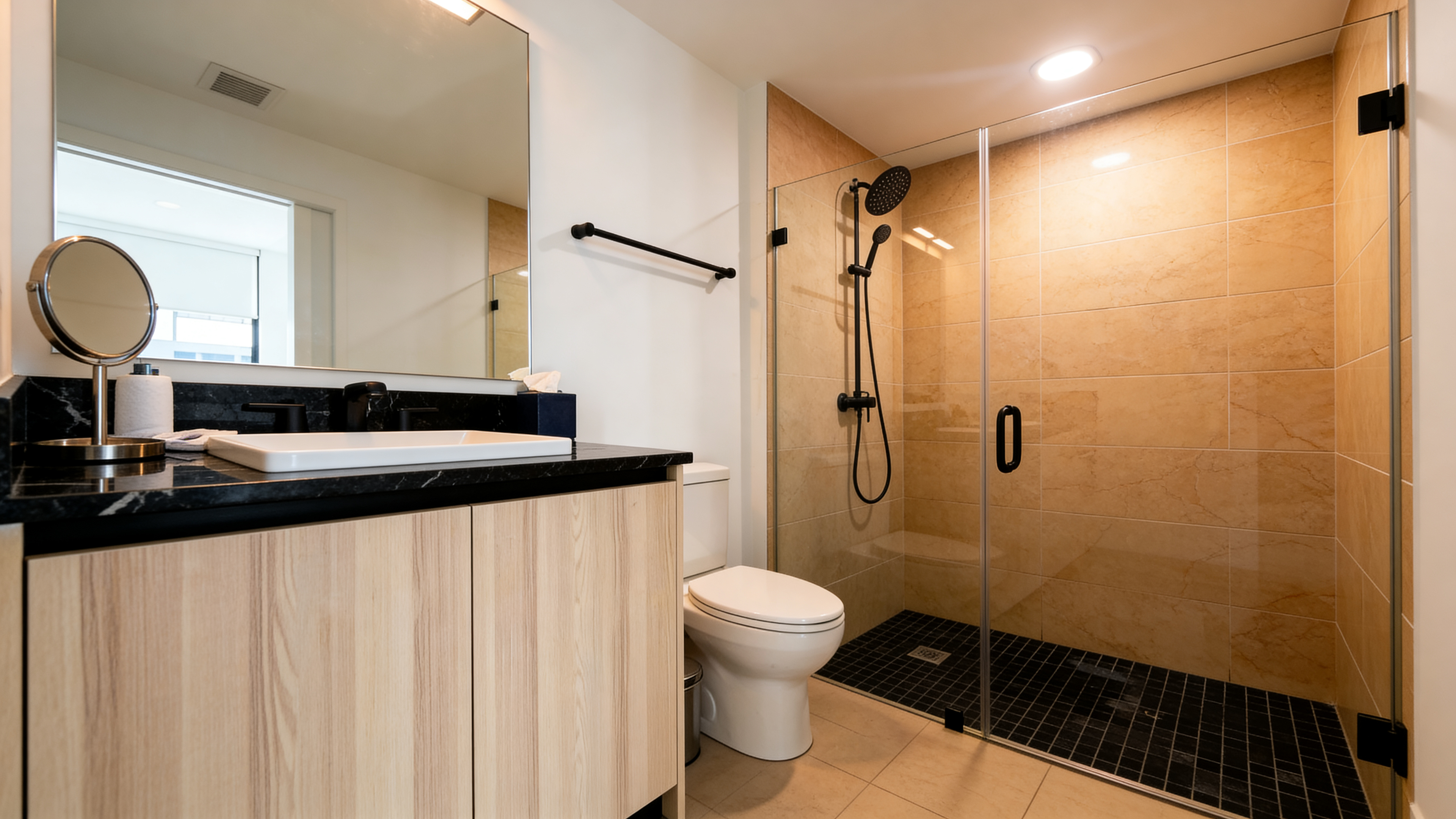 Primary bathroom — glass-enclosed shower, warm stone tile surround, matte black fixtures